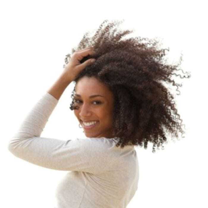 Smiling woman with curly hair, wearing a light shirt against a plain background.