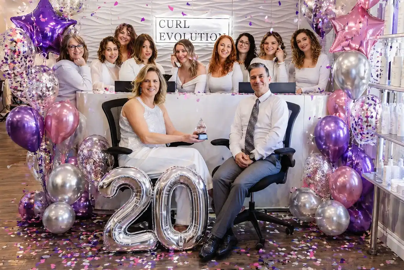 Salon team celebrating 20th anniversary with balloons and confetti in a festive setting.