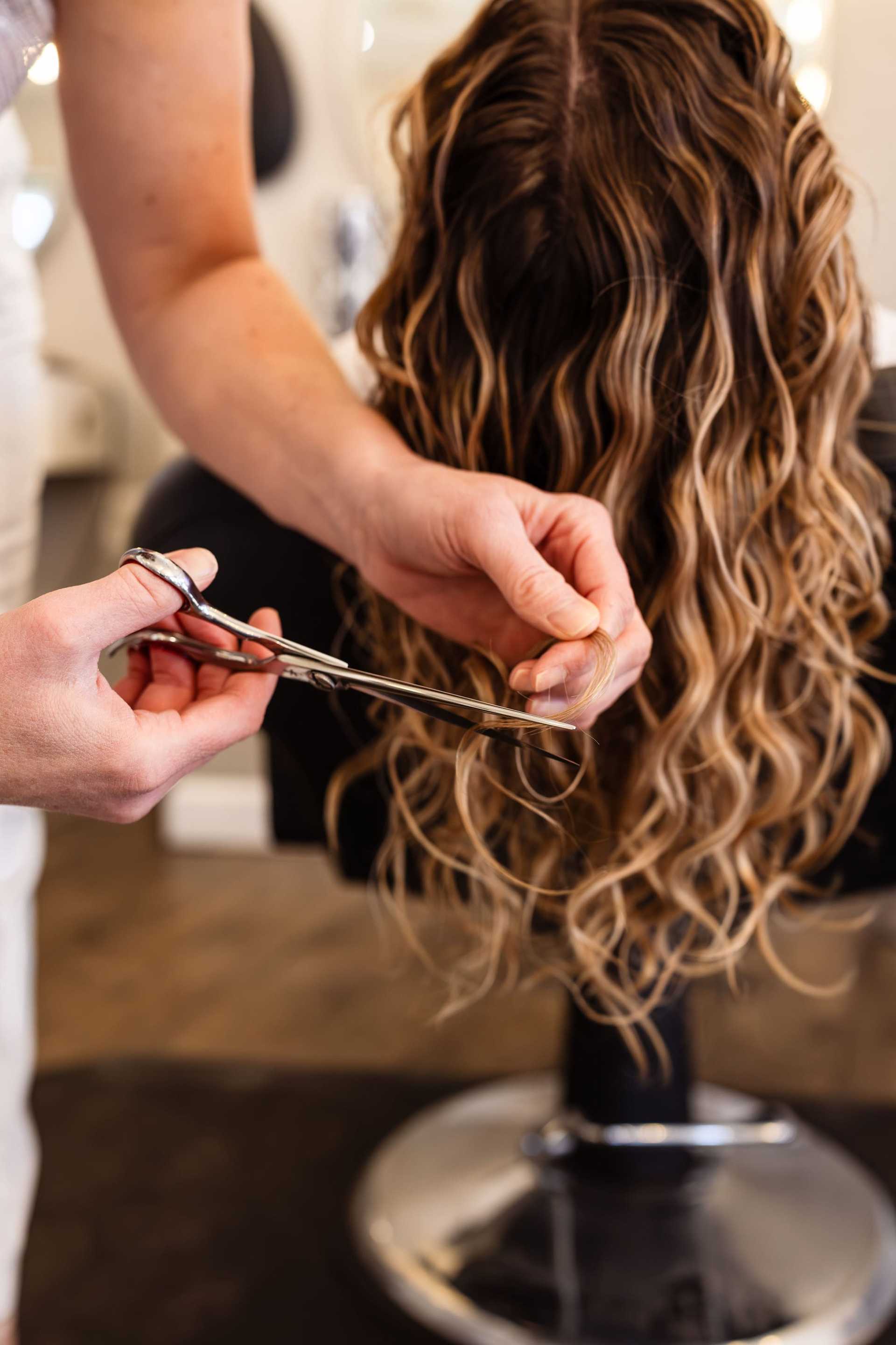 Hair stylist cutting wavy hair in a salon chair.